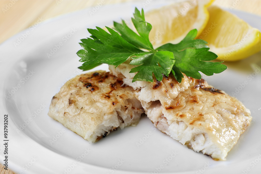 Dish of fish fillet with greens and lemon on plate close up Dish of fish fillet with greens and lemon on plate close up