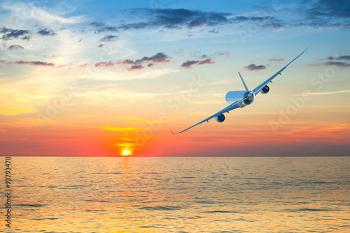 Jumbo jet airplane flying above tropical sea at beautiful sunset.