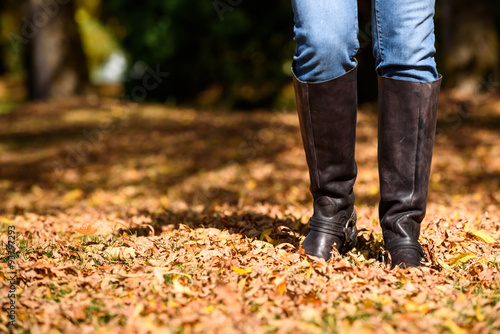 Woman walking through fall leaves, legs and feet only 