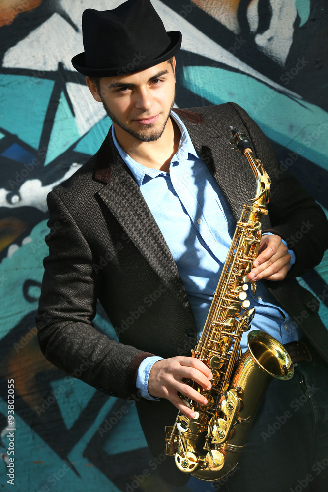 Naklejka premium Young man with saxophone outside near the old painted wall