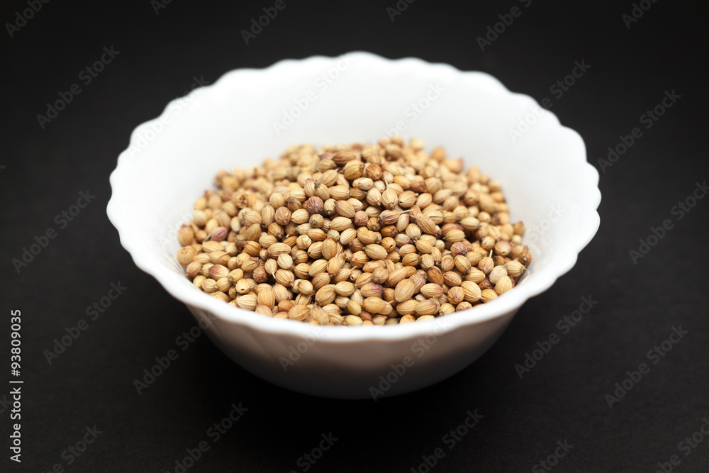 Organic Dried coriander seeds (Coriandrum sativum) in white ceramic bowl on dark background.