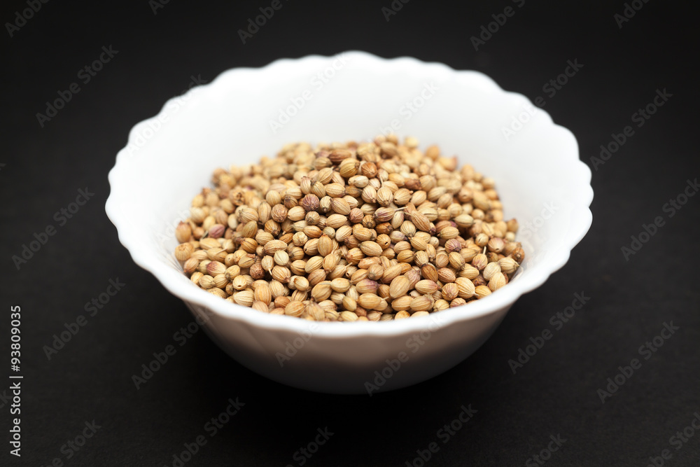Organic Dried coriander seeds (Coriandrum sativum) in white ceramic bowl on dark background. Organic Dried coriander seeds (Coriandrum sativum) in white ceramic bowl on dark background.