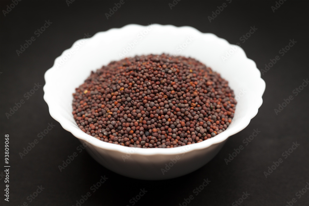 Organic brown mustard (Brassica juncea) in white ceramic bowl on dark background. Organic brown mustard (Brassica juncea) in white ceramic bowl on dark background.