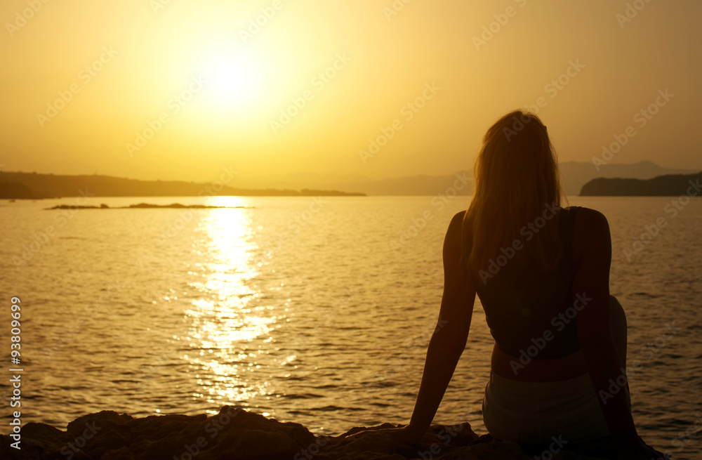 Silhouette of woman relaxing against sunset.