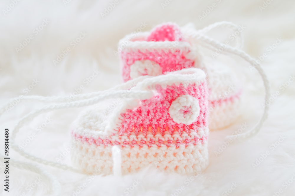 Little baby shoes. Hand knitted first sneakers for newborn girl. Crochet handmade pink bootees on fluffy white background. Stock Adobe Stock