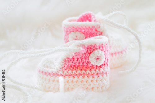 Little baby shoes. Hand knitted first sneakers for newborn girl. Crochet handmade pink bootees on fluffy white background.