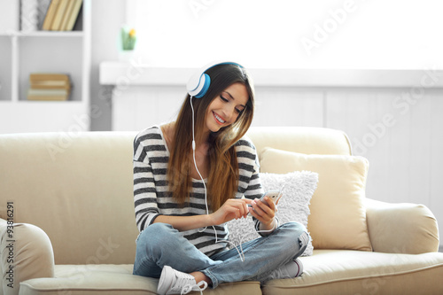 Woman listening music in headphones while sitting on sofa in room