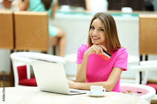 Beautiful young woman with laptop and credit card in cafe