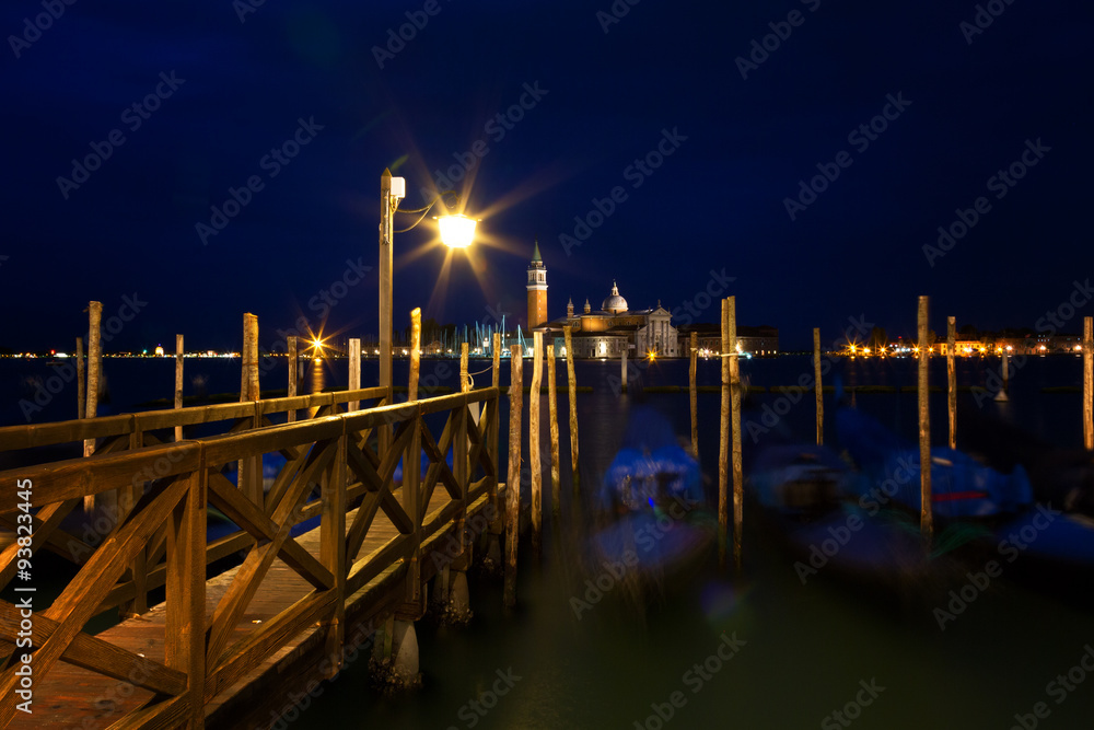 Gondolas at night near the wooden mooring with the burning lamp, Venice, Italy