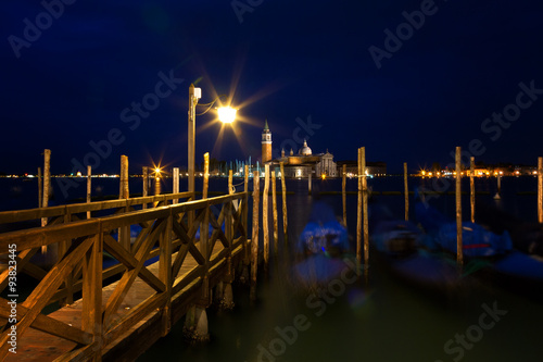 Gondolas at night near the wooden mooring with the burning lamp, Venice, Italy