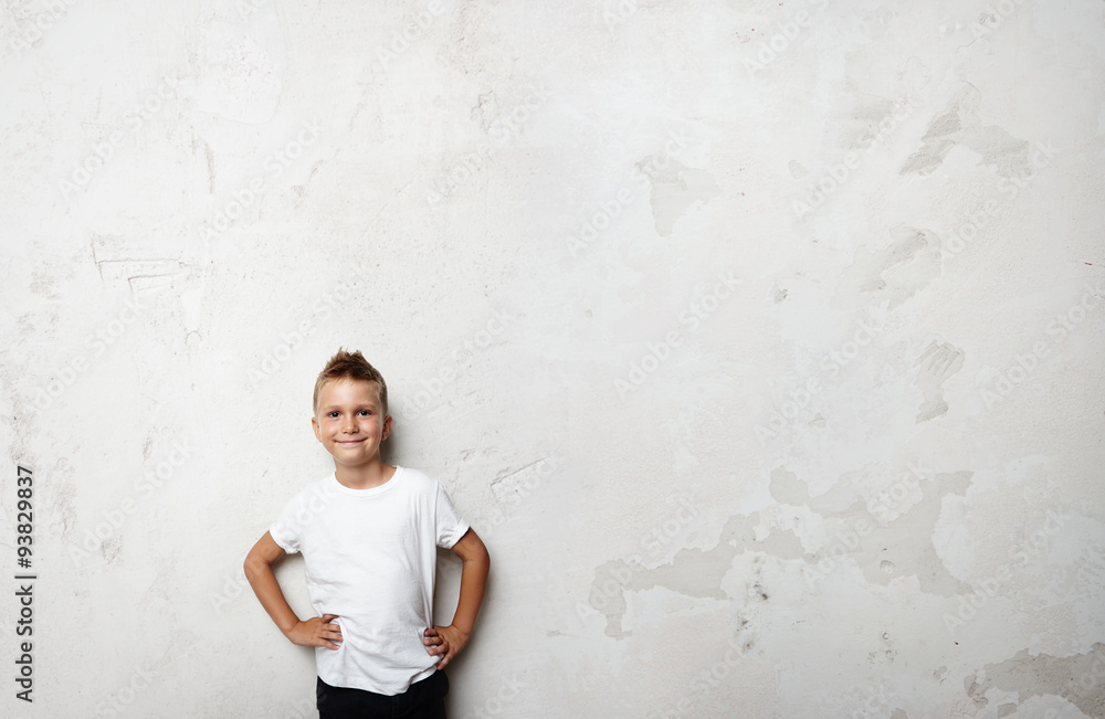 Young boy wearing white tshirt and smiling on the concrete wall Young boy wearing white tshirt and smiling on the concrete wall