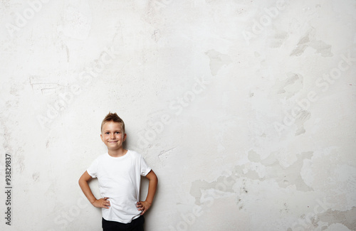 Young boy wearing white tshirt and smiling on the concrete wall