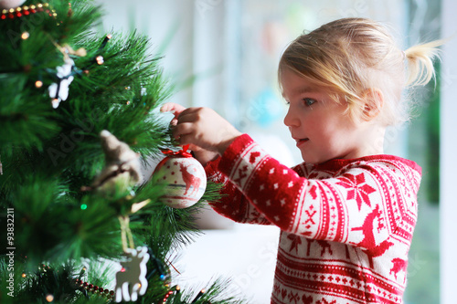 Little girl decorating christmas tree with toys and baubles. Cute kid preparing home for xmas celebration.