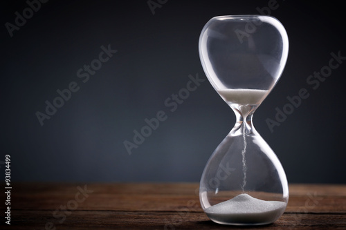 Hourglass on wooden table on grey background