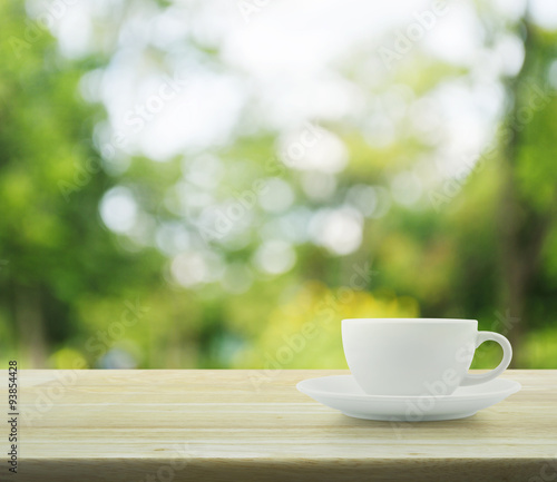 White cup on wooden table over tree bokeh background