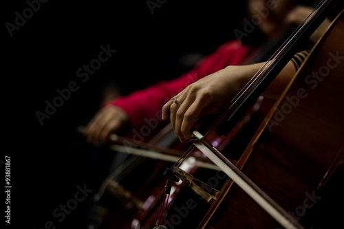 The hand of the girl playing the cello in the orchestra in dark colors