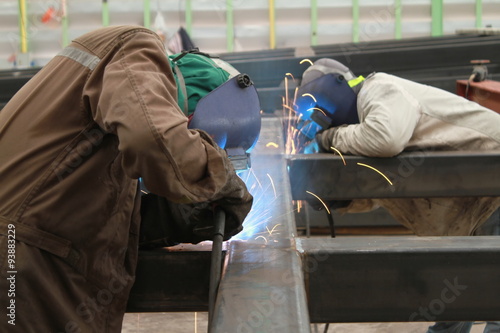 two welder are welding steel structure with all safety equipment in factory