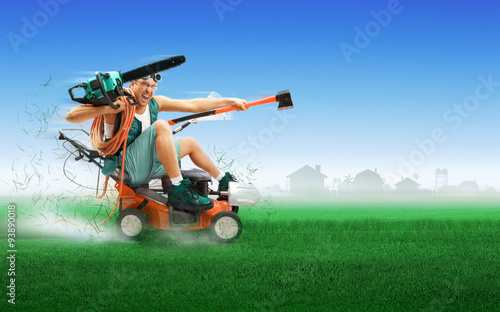 Crazy workman covered with instruments driving lawn mower over green grass photo