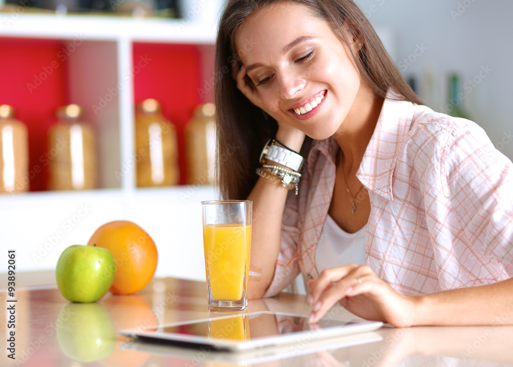 Woman using a tablet computer while drinking tea in her kitchen Woman using a tablet computer while drinking tea in her kitchen