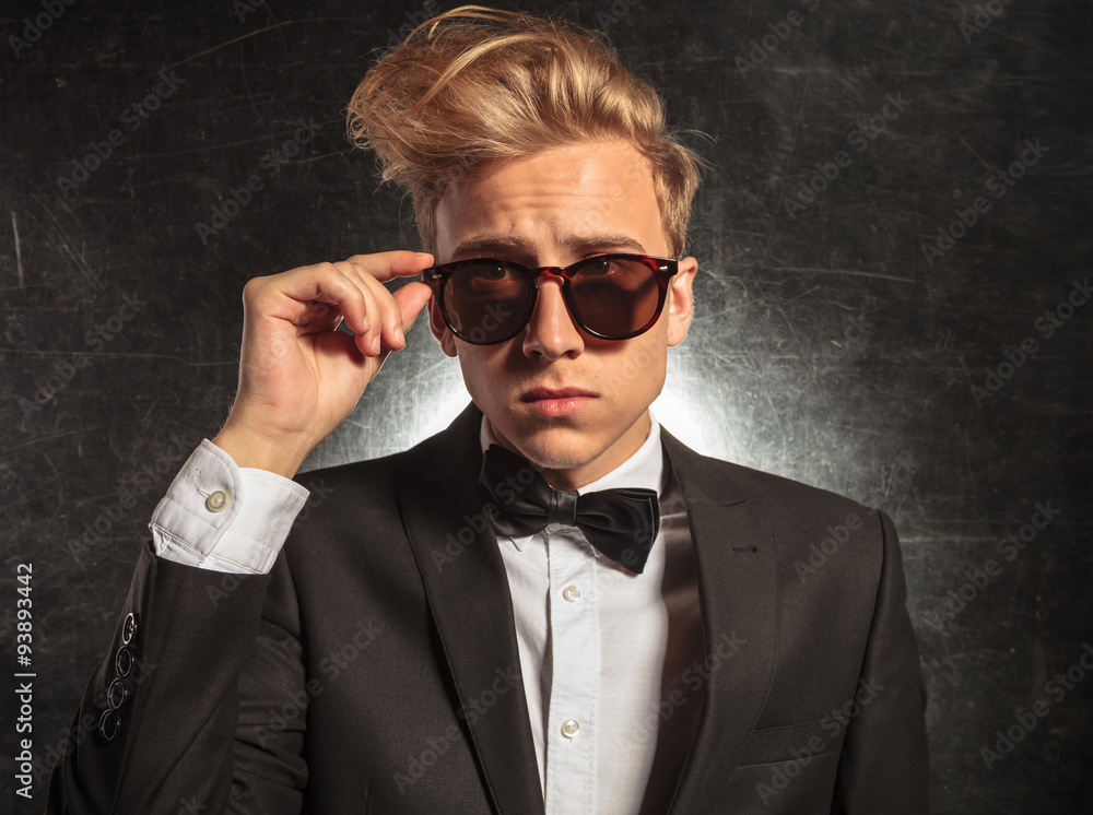 young man in studio wearing tuxedo while fixing sunglasses young man in studio wearing tuxedo while fixing sunglasses