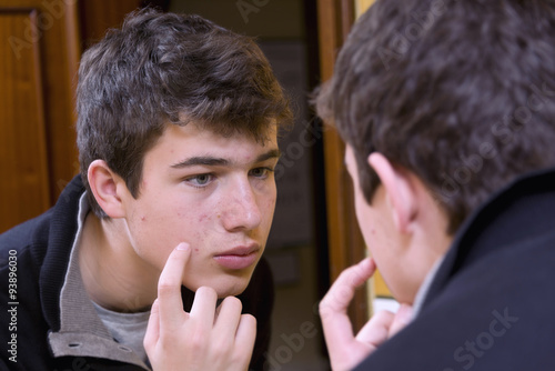 Teenager examining acne in the mirror photo