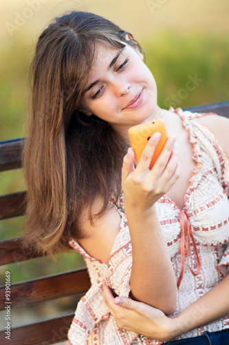 young beautiful woman with a phone on a park bench