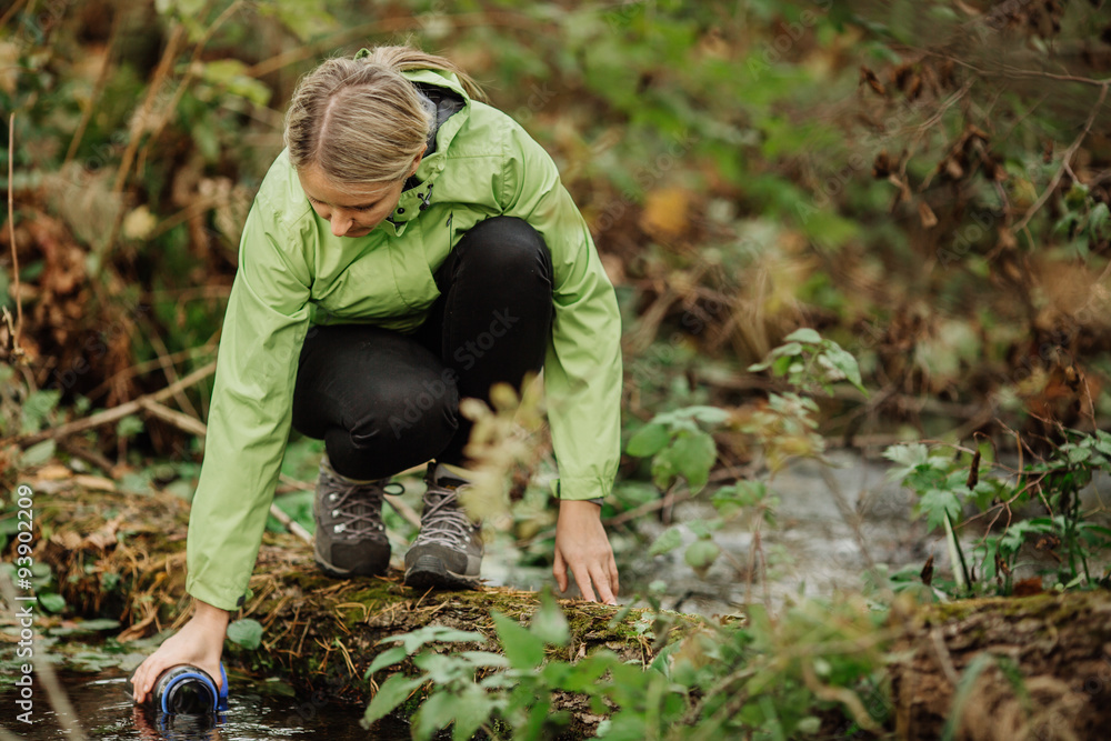woman taking water from forest spring on hiking trip woman taking water from forest spring on hiking trip