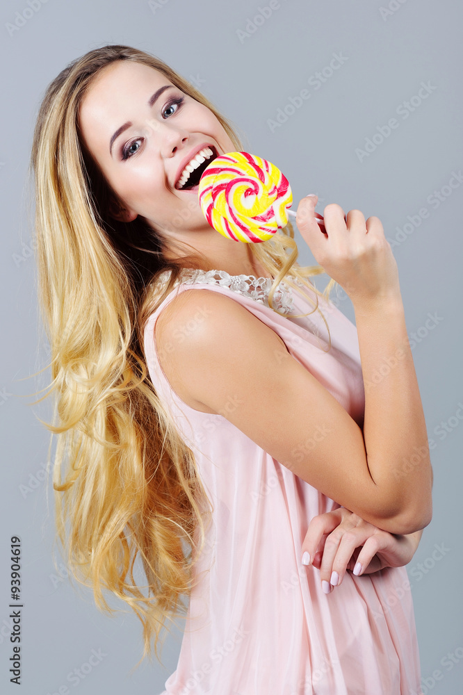 Portrait of a beautiful young woman with long hair tasting bright and colorful candy