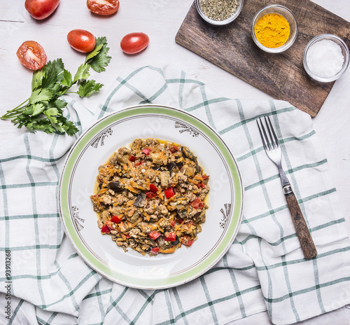 Georgian dish of lamb with eggplant and vegetables On a white plate with herbs and tomatoes and parsley with a fork on a checkered napkin on rustic wooden background top view photo