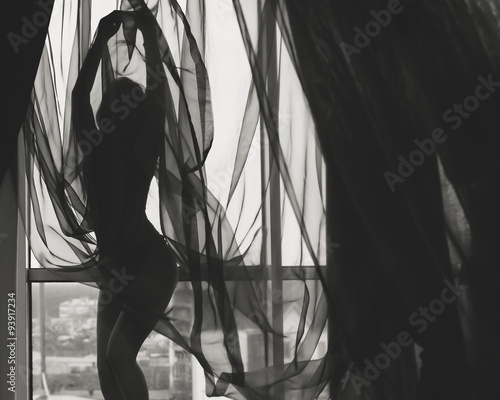 Black and white silhouette of beautiful young lady beside window