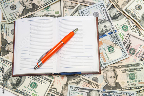 pen lying on open notebook with dollars background