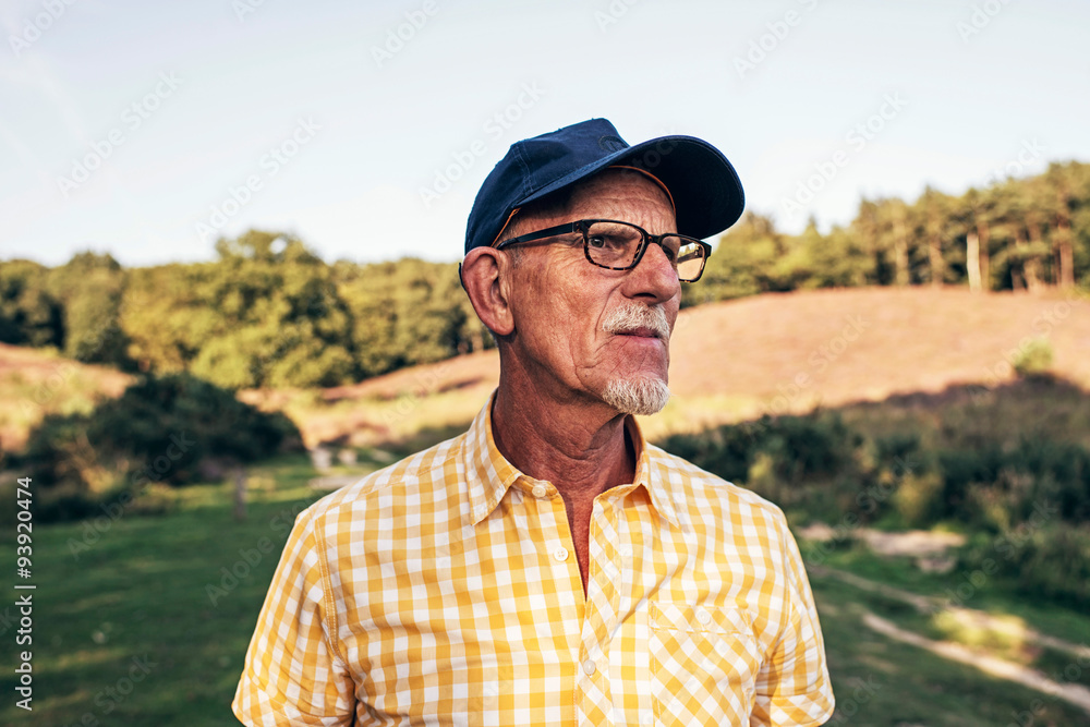 Senior man with beard and cap outdoors in park.