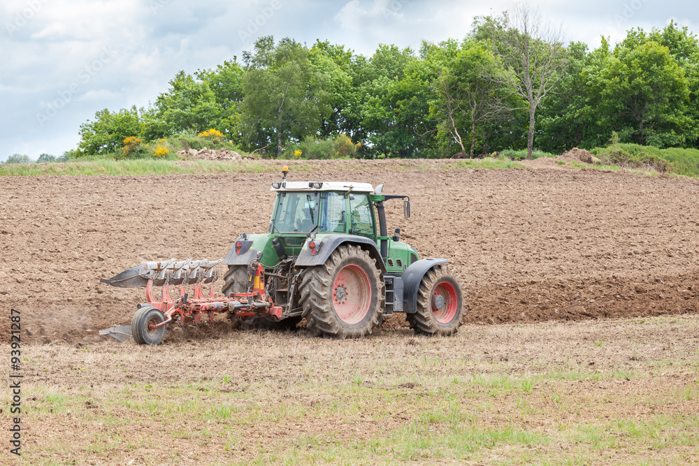Fototapeta premium Farmer ploughing a fallow agricultural field for planting with a tractor and plough preparing the soil for the planting of the spring crop.