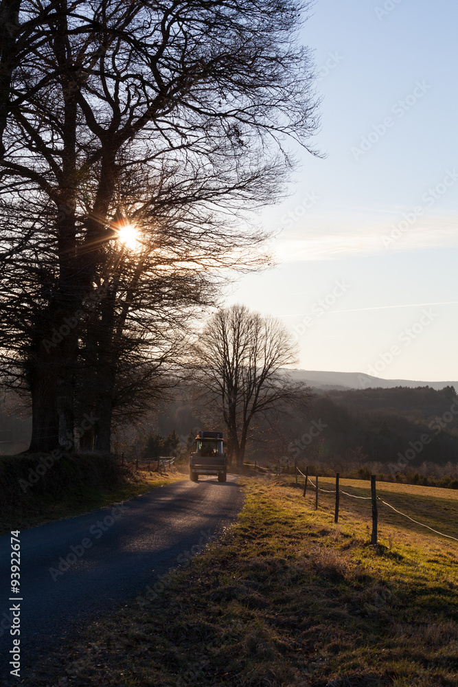 Farmer going home after a long day driving his tractor along a mountainous farm road at sunset in winter Farmer going home after a long day driving his tractor along a mountainous farm road at sunset in winter