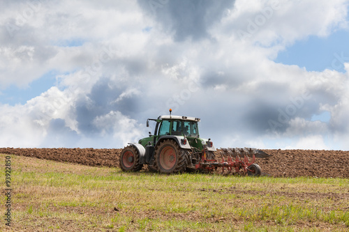 Farmer ploughing an overwintered field ready for planting the spring crop  against a dramatic cloudy sky using a tractor and plough