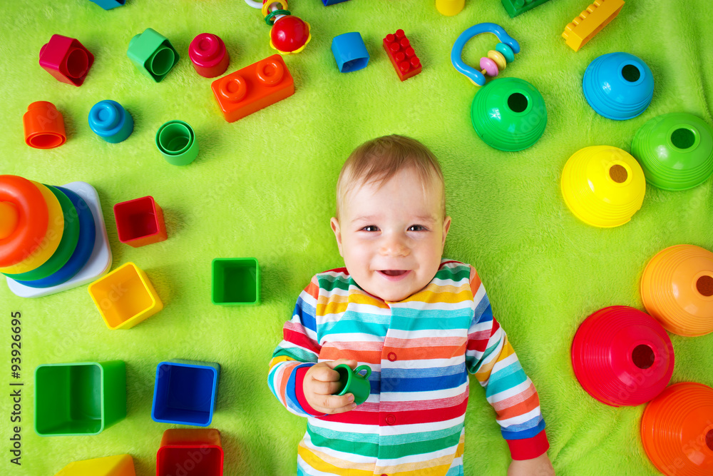 Obraz premium Baby boy lying on the blanket with many toys around