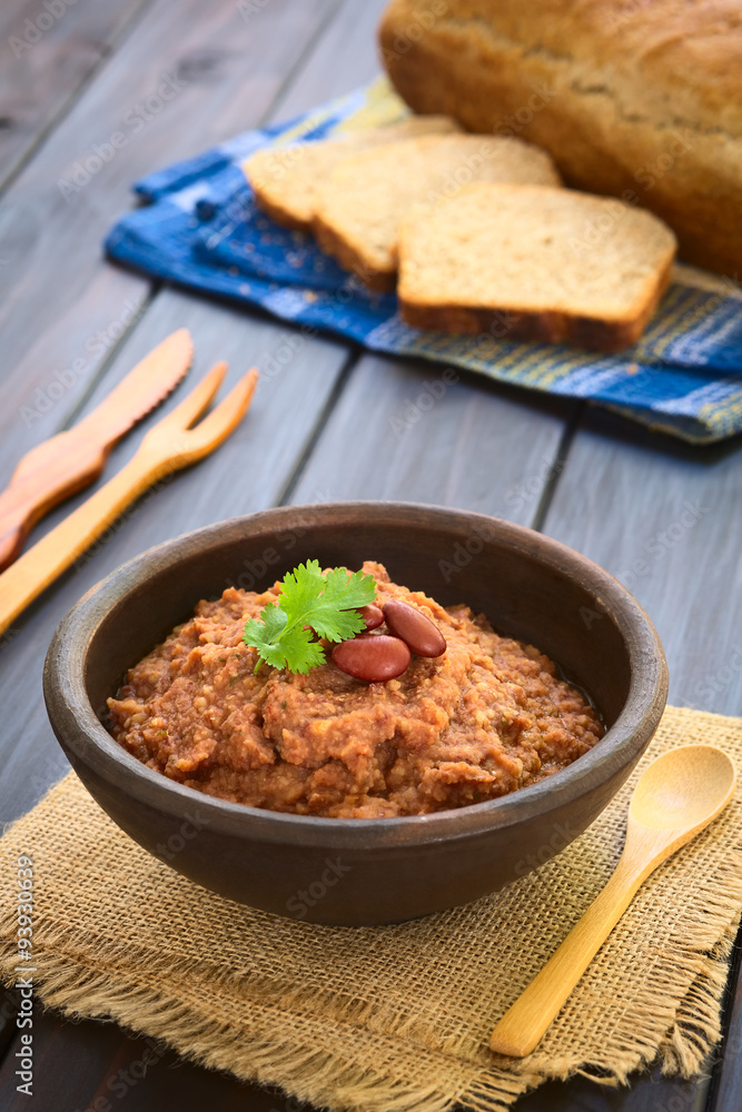 Homemade red kidney bean spread garnished with kidney beans and fresh coriander leaf, wholegrain bread in the back, photographed with natural light (Selective Focus, Focus on the leaf)