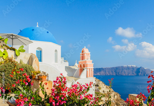 Blue dome of church on Santorini island in the early morning with tropical flower plant and yellow sunlight, Mediterranean sea, Greece