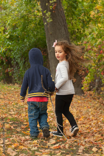 two young children walking in a park dragging together a long © zoeytoja