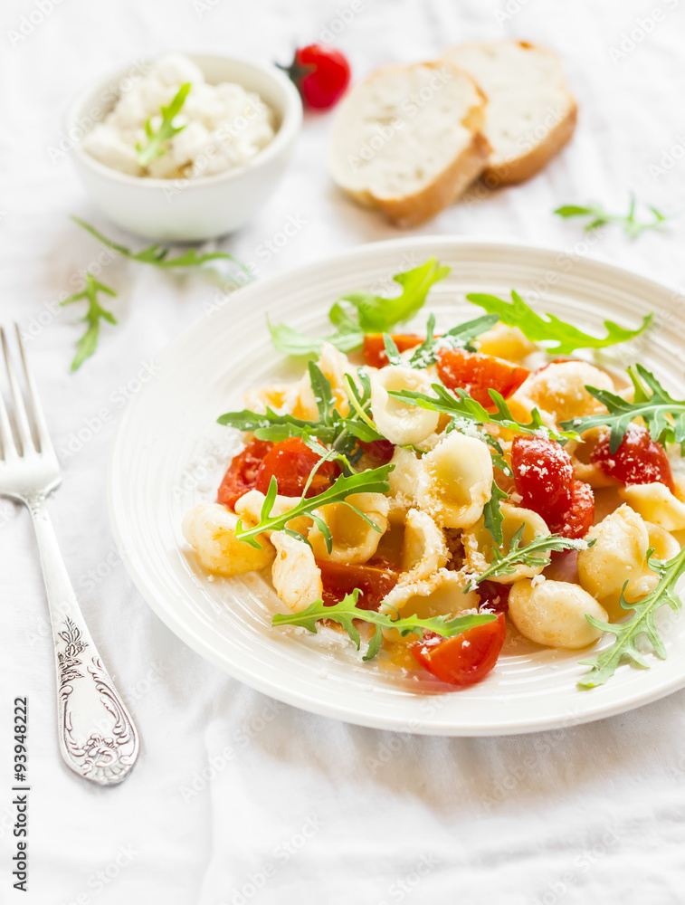 Orecchiette pasta with cherry tomatoes, arugula and Parmesan for a bright plate on a white surface Orecchiette pasta with cherry tomatoes, arugula and Parmesan for a bright plate on a white surface