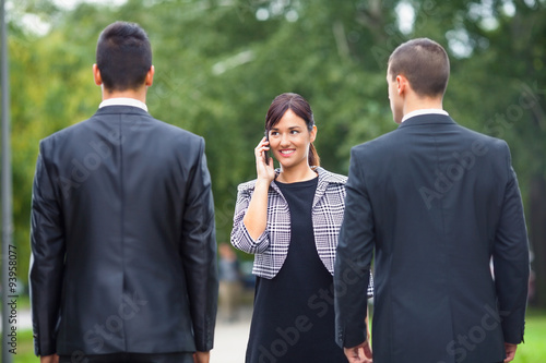 Smiling young businesswoman talking on the phone while meeting two businessmen on the street