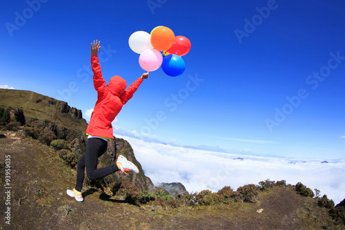 cheering young woman running on mountain peak with colorful ball