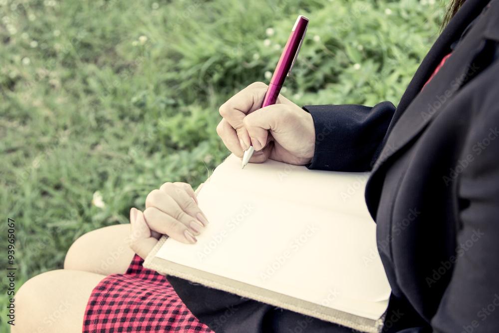 Woman hand writing her notebook in the garden,vintage filter
