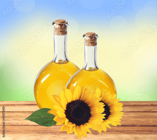 oil in bottles and sunflowers on wooden table over nature backgr