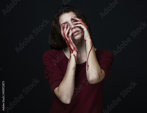 Scary Girl and Halloween theme: portrait of a crazy girl with a bloody hand covers the face in studio on a dark background, bloody tears