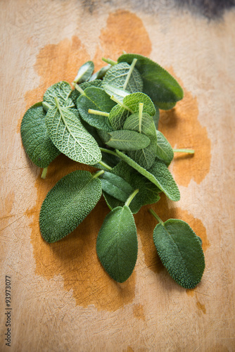 Italian sage leaves on wooden cutting board with water stains (top view) 