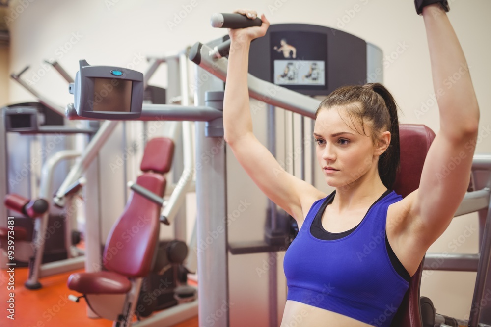 Fototapeta premium Fit woman using weights machine for arms