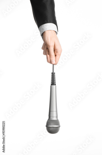 Business and speech topic: Man in black suit holding a gray microphone on an isolated white background in studio