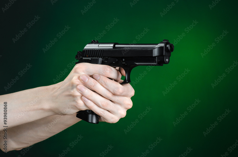 Firearms and murderer topic: human hand holding a gun on a dark green background isolated in studio