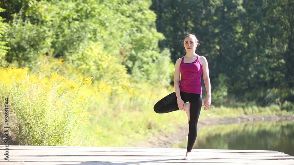 Young beautiful woman in red tank top practicing outdoors, doing Tree posture (Vrksasana) in park on summer day Young beautiful woman in red tank top practicing outdoors, doing Tree posture (Vrksasana) in park on summer day